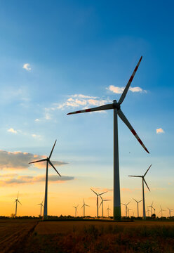 Wind turbines against sunset sky. Wind turbines stand tall in a field during sunset with colorful clouds in the sky and fields in the foreground.