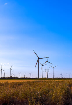 Wind turbines on field in sunny weather. Wind turbines stand tall in a field under a clear blue sky during daytime. Grass grows around the bases of the turbines.