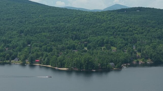 Aerial view of pontoon motorboat cruising by lakeshore cottages and cabins in the mountains of northern New England