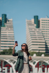 Fototapeta premium Woman taking selfie with smartphone in city, enjoying urban lifestyle and coffee while traveling