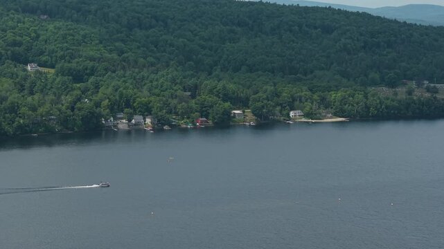 Aerial footage of pontoon boat making way by two kayaks on lake in northern Vermont 