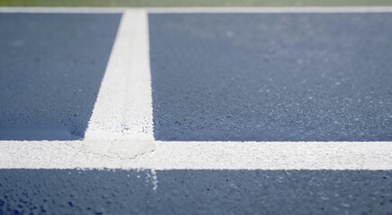 Fototapeta premium Close up of white boundary lines on a blue hard tennis court. Textured sports surface background with selective focus