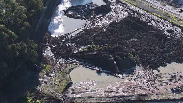 High angle view of a construction site with excavator moving large piles of dirt and mud