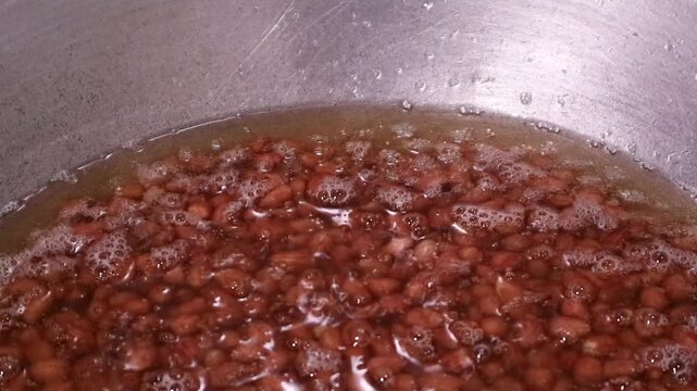 Red kidney beans boiling in a metal pot with water.