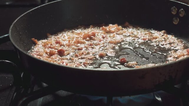 Diced pancetta sizzles and crisps in a skillet on a stovetop