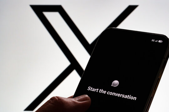 XChat welcome screen shown on a smartphone held in hand against a large X logo on a monitor. Stafford, United Kingdom, August 2, 2026.