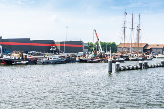 Traditional working boats and a historic tall sailing ship moored beside maritime workshops in the harbor of Harderwijk, the Netherlands.