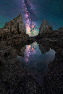 Milky Way rising above coastal cliffs and tidepool reflection