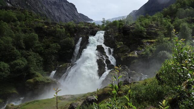 Powerful waterfall rushing over rocks with glacier view in Norway