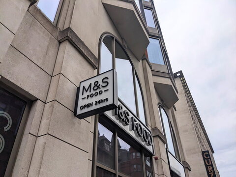 Low angle view of the M and S Food shop sign on Coventry Street in central London under a cloudy sky