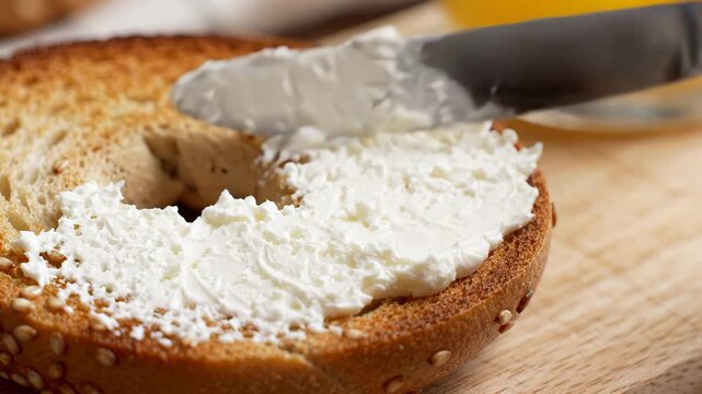 Spreading cream cheese onto a toasted sesame seed bagel in close-up