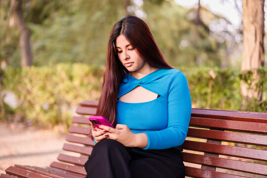 Gen z latina woman relaxing using smartphone in park