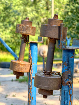 Old iron dumbbells with hanging chains placed on blue racks in an outdoor fitness area for bodybuilding, strength exercises and workout activities