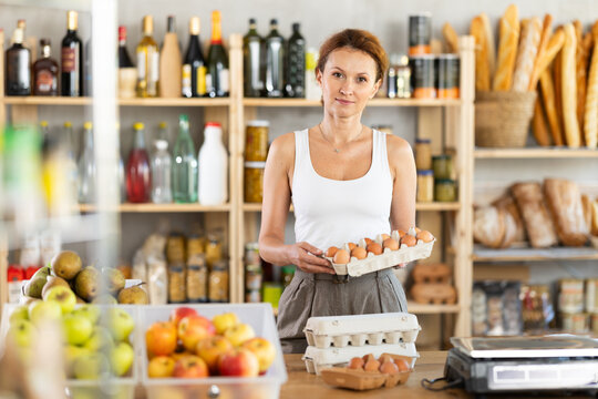 Adult female seller at counter offering packaged eggs in grocery store
