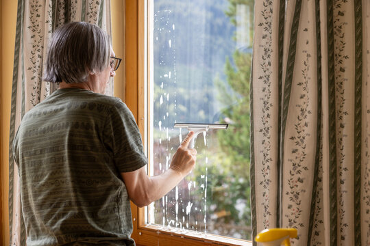 Mature man clean apartment window with squeegee indoors