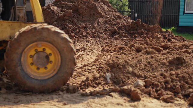 Heavy earthmoving equipment moving soil and clay while leveling the landscape on a construction site. The bulldozer's large wheel spins, leaving tracks on the muddy ground during earthworks