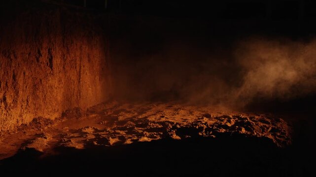 Incandescent stream of molten iron flowing from a blast furnace in a dark metallurgical plant, creating a cloud of steam and smoke while solidifying into a pig iron bed