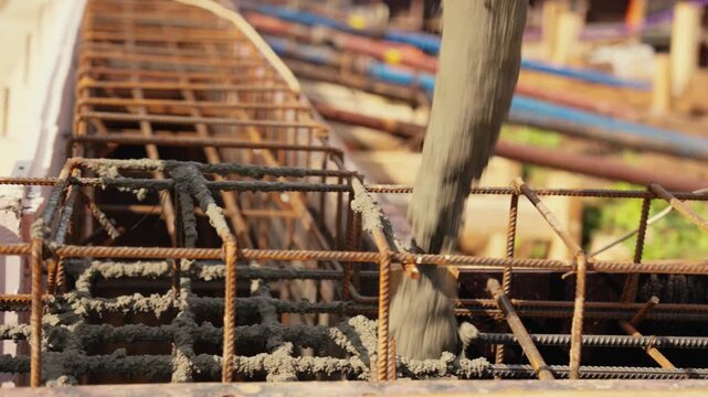 Liquid cement mixture pouring into a reinforced concrete structure with steel bars on a building construction site. The industrial process of creating a solid foundation for a new house