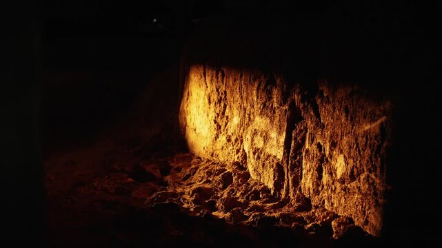 Warm glow from a moving torch illuminating the textured surface of a rugged rock wall in a dark, mysterious underground cave, creating an atmosphere of adventure and discovery