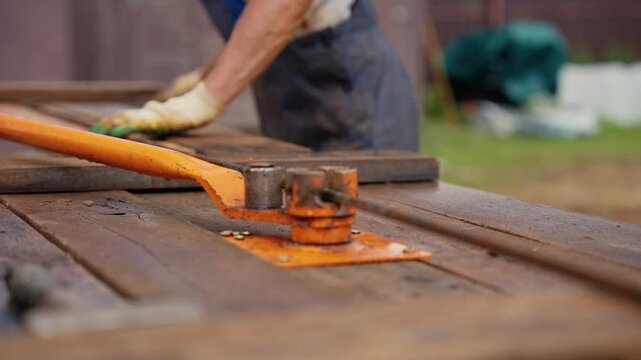 Industrial worker in protective gloves bending steel reinforcing bars using a manual machine on a wooden table