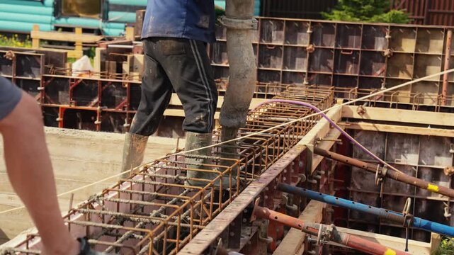 Professional builder pouring wet cement mix from a pump hose into a reinforced steel rebar cage at a residential building construction site, creating a solid monolithic foundation for a new house