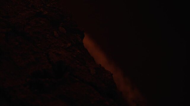 Glowing hot lava flowing down the side of a volcanic crater during a nighttime eruption, with smoke and steam rising into the dark sky, showcasing a powerful and dangerous natural event