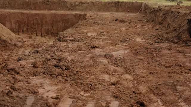Deep foundation pit dug in the ground for a new building construction project, revealing layers of earth and soil at an industrial development site before concrete pouring begins