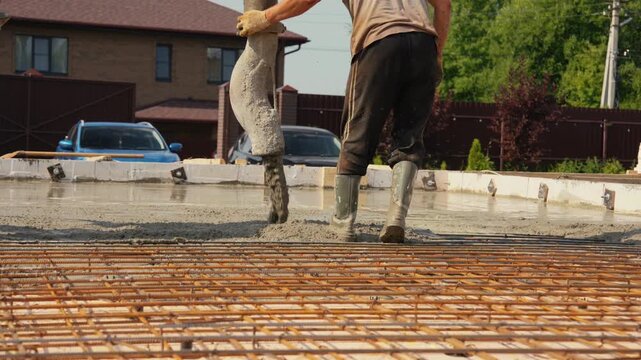 Professional builders using a concrete pump to pour a wet cement mix over a rebar grid, creating a solid monolithic slab for a new house foundation at a construction site outdoors