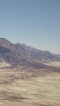 The scene shows a wide view of mountains under a clear sky. The ground has a dry appearance with little vegetation. The setting looks remote and expansive.