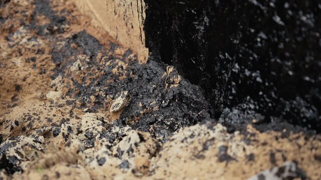 Black, viscous crude oil seeping into the sand, causing severe environmental contamination. Industrial waste and toxic petroleum polluting the soil, resulting in an ecological disaster