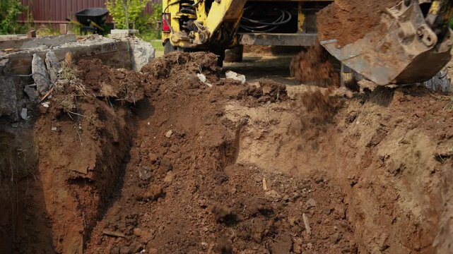 Heavy machinery at a construction site digging a deep trench for a building foundation or pipeline installation, with the backhoe bucket moving earth and soil in an industrial excavation project