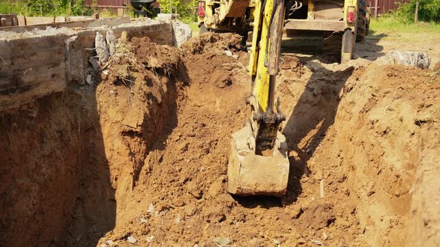 Yellow excavator machinery filling a large pit with soil during earthworks on a sunny construction site, preparing the ground for the foundation of a new building in slow motion