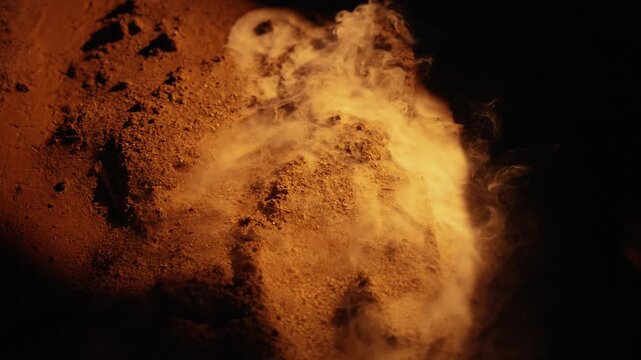 Billowing white vapor rising from a pile of warm, orange toned sandy earth against a black background, creating an eerie and mysterious atmospheric effect resembling a volcanic planet