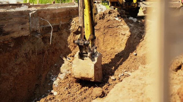 Heavy machinery with a mechanical shovel digging a deep pit for building foundations during earthworks, moving soil and dirt on a sunny day at a new residential construction site