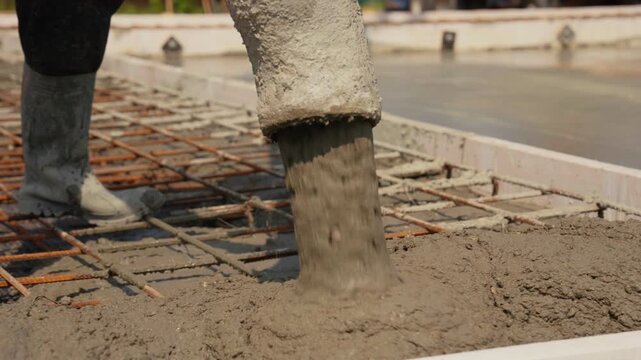Industrial construction site showing a concrete pump pouring wet cement mixture over a reinforced steel grid to create a solid and durable building foundation for a new structure