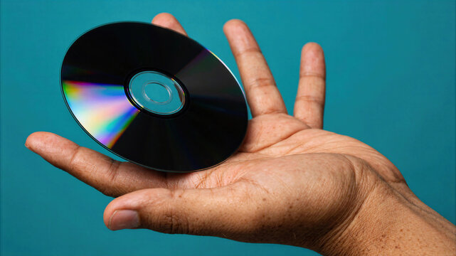 Close-up of a person holding a blank compact disc in their hand against a solid blue background
