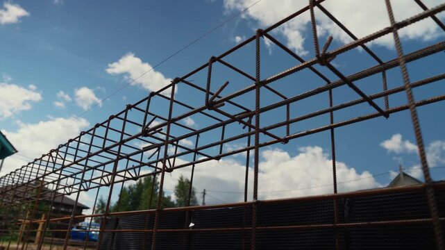Low angle view of a reinforcing steel bar framework against a blue sky with clouds. Rusty rebar structure prepared for concrete pouring on a building site, representing new home foundation work