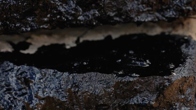 Dark liquid bitumen dripping from a roof during waterproofing and insulation work, creating a thick, sticky layer of tar to protect the surface from water damage and weather elements