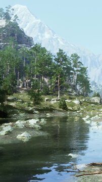 A river flows through a rocky area surrounded by green trees and tall mountains. Snow can be seen on the peaks in the background. The scene is bright and clear, showing nature.