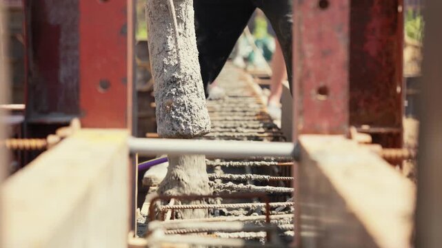 Close up view of a concrete pump hose pouring liquid cement into a reinforced steel rebar cage at a construction site, creating a solid foundation for a new building or structure