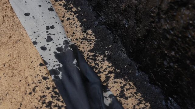 Hot liquid bitumen spreading over sand and a masking tape line during road construction, a detailed top down view of the waterproofing and sealing process creating a protective layer