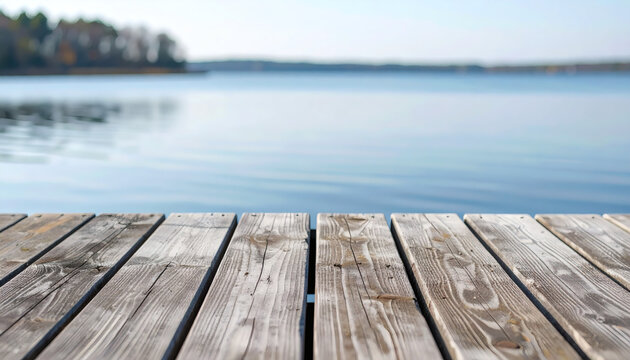 Wooden pier planks overlooking a calm blue lake with soft natural daylight and a blurred forest background in early autumn
