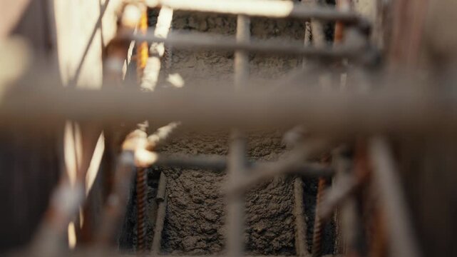 Freshly mixed cement pouring into a trench with a rebar cage at a construction site, creating a solid reinforced concrete footing for a new building foundation under the sunlight