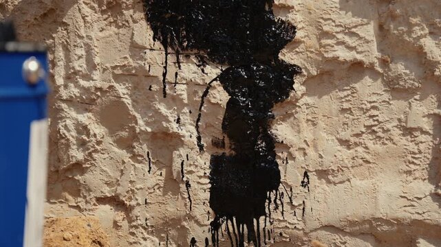 Close up of a builder applying black mastic with a brush to a concrete foundation wall for damp proofing and waterproofing, ensuring structural integrity and protection against moisture