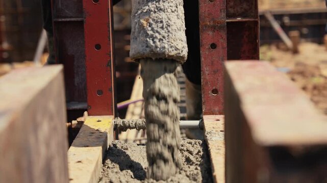 Heavy industrial machinery pouring fresh, liquid concrete from a hose into a reinforced formwork during the foundation phase of a construction project, creating a solid base for a new building