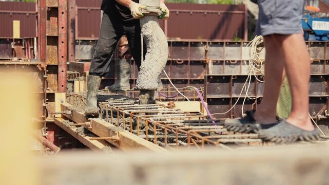 Builders pouring wet cement mix from a pump truck hose into the reinforced steel cage of a house foundation, creating a solid base for the building and ensuring structural integrity