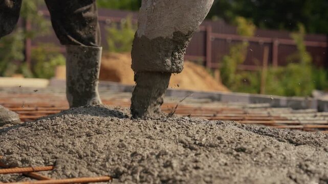 Close up view of a concrete pump hose pouring liquid cement mix over a rebar enforced grid during the foundation construction phase of a building project in slow motion