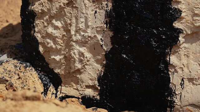 Professional construction worker applying a thick layer of black bitumen mastic with a brush for foundation waterproofing. Ensuring protection against moisture and extending the building's durability