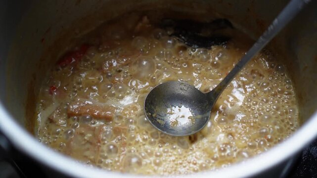 Rich bubbling curry simmering in pot with spoon resting inside featuring chunks of meat and spices for authentic culinary use, featuring intricate cooking details.