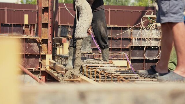Construction workers using a concrete pump to pour wet cement into a reinforced steel formwork during the foundation phase of a building project, creating the base for a new structure